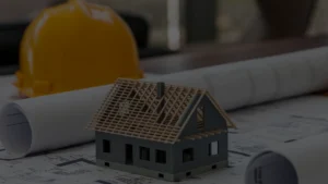 Miniatura de casa em construção representando retrofit com capacete amarelo ao fundo