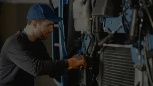 Homem de capacete executando a manutenção mecânica de um equipamento ou máquina.