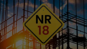 Imagem de canteiro de obras com andaime e uma placa amarela escrito "NR-18".
