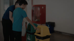 Pessoa orientando uma criança no descarte correto de resíduos em lixeiras seletivas, representando a educação ambiental e a aplicação do PGRS em ambientes escolares.