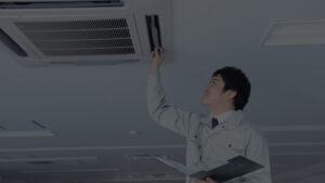 Técnico realizando inspeção e manutenção em sistema de climatização comercial instalado no teto de um ambiente corporativo