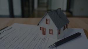 Legalização imóvel: maquete de uma casa sobre documentos de regularização imobiliária e contrato de propriedade.